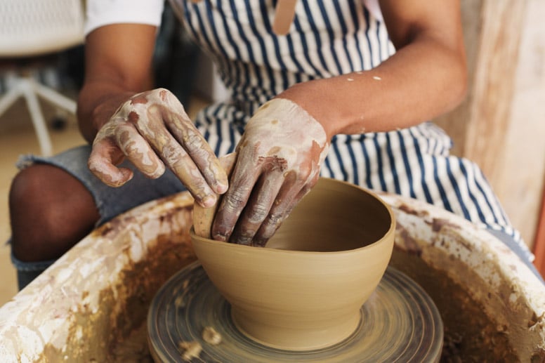 Ceramic artist shaping a clay bowl on a potter's wheel, hands covered in clay, focused on pottery creation.