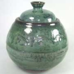 Glazed green pottery jar with a lid, featuring intricate texture and vibrant glossy finish, ideal for decorative purposes.