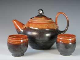 Ceramic teapot and two cups with a black and orange glaze, showcasing functional pottery design and glazing techniques.