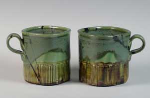 Two handcrafted stoneware mugs with a green glaze and textured base, showcasing clay crafting techniques and finishing.