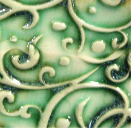 Close-up of a ceramic tile featuring an intricate green glaze with swirling patterns and raised designs.