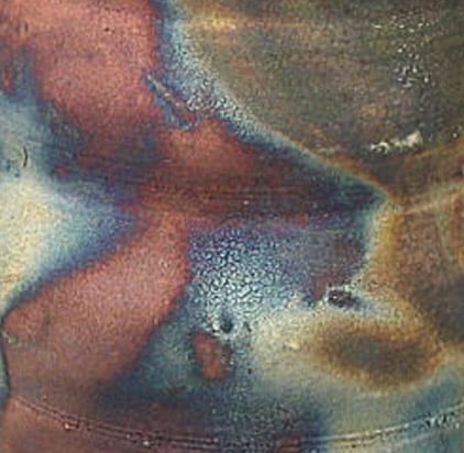 Close-up of a ceramic surface showcasing vibrant, mixed glazes in rich shades of blue, red, and gold after kiln firing.