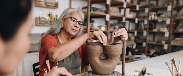 A potter shapes a clay sculpture in a ceramics studio, surrounded by tools and materials for pottery and glazing.