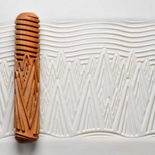 Textured clay surface with a decorative wooden rolling pin, showcasing patterns for pottery and ceramic decoration.