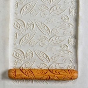 Embossed white clay slab with leaf patterns, using a textured wooden rolling pin. Ideal for pottery decoration techniques.
