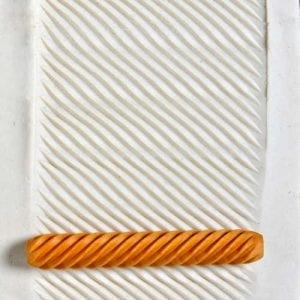 Orange sculpting ribbon tool resting on a white textured clay surface with diagonal lines, ideal for pottery decoration.