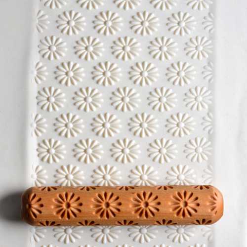Textured white clay slab with floral impressions created using a carved rolling pin resting on top.