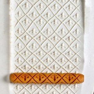 Textured white clay slab with detailed embossed floral patterns and a wooden clay roller lying horizontally on top.