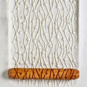 Textured white clay slab with decorative slip trailing, featuring a wooden texture roller, ideal for pottery techniques.