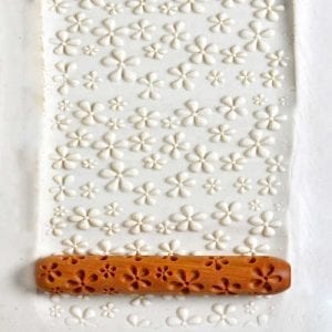 Embossed clay slab with floral patterns, rolled using an intricately carved wooden roller for decorative pottery work.