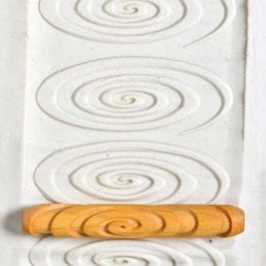 A white clay slab featuring spiral impressions created using a wooden trimming tool, ideal for pottery techniques.