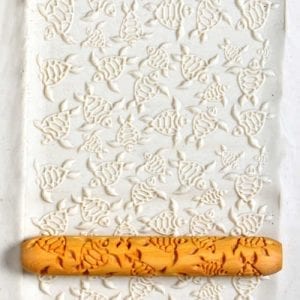 Textured white clay slab with a fish pattern rolled into the surface using a decorative ceramic roller.