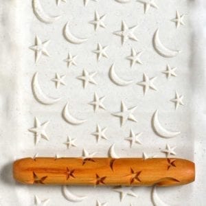 A rolling pin with star designs rests on textured clay, featuring embossed stars and moons, ideal for ceramic projects.