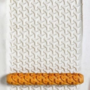 A white clay slab textured with a star pattern, rolled with an orange ceramic texture stamp for decoration.