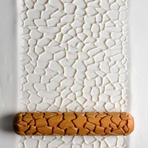 Textured white clay slab with a wooden rolling tool, showcasing an intricate crackle pattern for ceramic decoration.