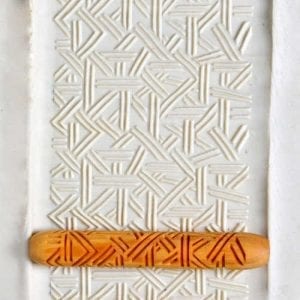 Textured white clay slab with an intricate pattern, featuring an orange pottery roller for creating decorative impressions.