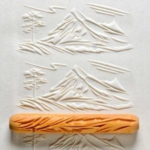 Embossed clay landscape showing mountains and trees, with a textured rubber roller on a cream-colored slab.
