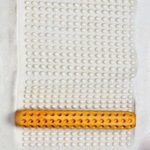 Textured white clay slab with an orange, dotted texture rolling pin used for shaping pottery at Georgies Ceramics.