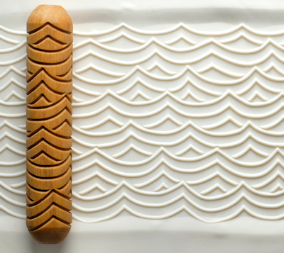 Wooden texture roller on white clay, creating wave patterns for pottery decoration, showcasing ceramic design techniques.