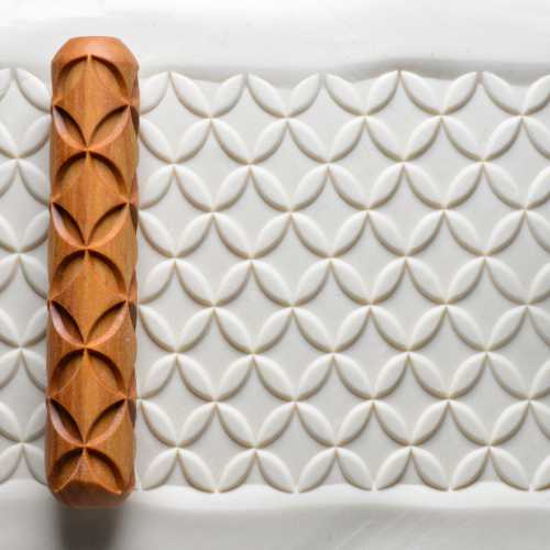 Wooden texture roller beside impressed clay with repeating oval and petal patterns, ideal for pottery decoration.