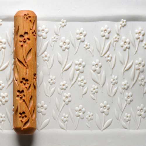 Decorative clay roller with floral design presses into white clay slab for pottery decoration at Georgies Ceramic & Clay Company.