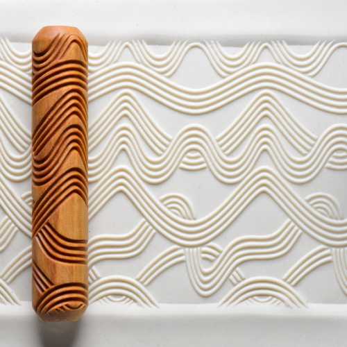 Wooden pattern roller resting on textured clay surface, featuring wavy designs; ideal for pottery decoration and sculpture.