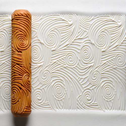 Textured white clay surface with intricate spiral patterns, alongside a decorative rolling pin from Georgies Ceramic & Clay Company.
