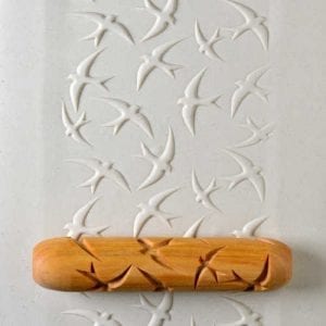 Textured clay slab with white bird impressions and a wooden stamp tool used for decorating ceramics.