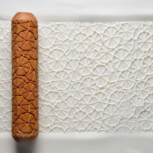 Textured pottery roller creates intricate patterns on clay surface, ideal for decorating ceramics at Georgies Ceramic & Clay Company.