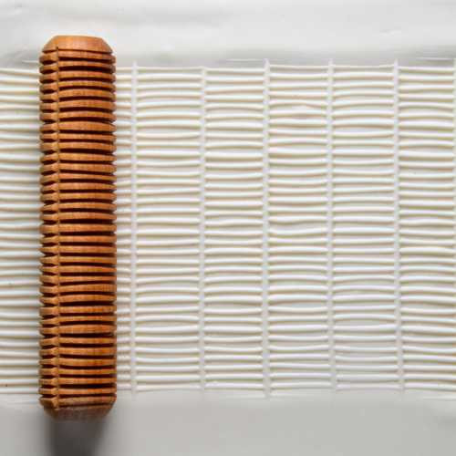 Textured rolling pin resting on white clay surface, used for creating patterns in ceramics and pottery projects.