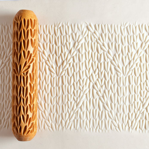 Textured clay slab with a decorative rolling pin, showcasing intricate leaf patterns for ceramic hand-building.