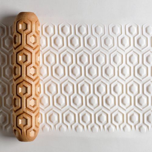 Textured pottery roller with hexagonal pattern beside an embossed clay surface, ideal for ceramic decorating techniques.