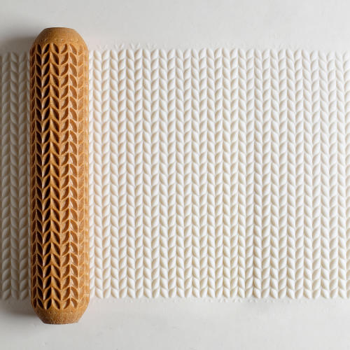 Textured clay surface being rolled with a decorative clay roller, showcasing a leaf pattern for pottery embellishment.