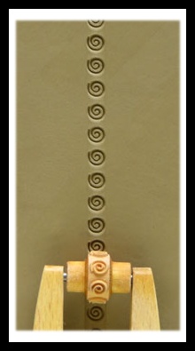 A close-up of a wooden texture roller creating spiral impressions on smooth clay, showcasing decorative pottery techniques.