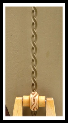 Clay ribbon with a braided design displayed on a textured surface, showcasing ceramic decorating techniques and tools.