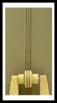 Wooden clay tool for adding texture to pottery, positioned against a background of unglazed clay with vertical lines.