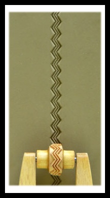 Wooden clay texture roller displaying a zigzag pattern pressed into smooth, green clay slab used for pottery decoration.