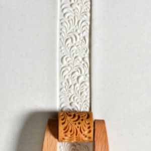 Embossed white clay ribbon with decorative swirls, paired with a wooden carving tool for pottery detailing.