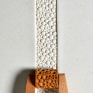 Textured white clay strip with a wooden handle, showcasing a bubbling surface pattern typical in ceramic design.