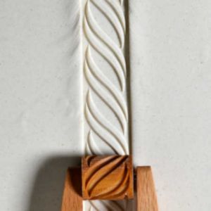 A textured clay piece featuring a swirling design, crafted with a wooden clay tool for pottery decoration.