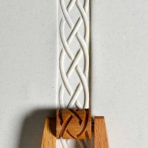 White ceramic strip with an intricate braided texture, held by a wooden pottery tool, showcasing decorative clay techniques.
