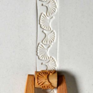 Embossed clay strip featuring leaf patterns, used for decorative pottery techniques, with a wooden texture tool for details.