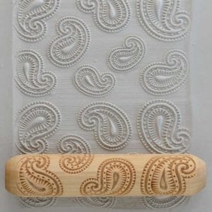 Embossed clay sheet with paisley pattern and wooden texture roller, perfect for ceramic decorating techniques.