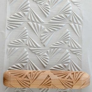 Textured white clay sheet featuring a geometric pattern, with a patterned wooden rolling pin on top, used for clay decoration.