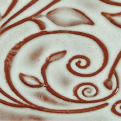 Ceramic surface featuring intricate brown leaf and swirl designs on a white glossy glaze, showcasing decorative pottery techniques.