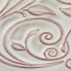 Detailed close-up of an embossed ceramic surface featuring swirling leaf motifs, highlighted with a reddish underglaze.
