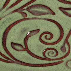 Detail of a green ceramic surface with intricate red decorative leaves and swirling patterns, showcasing glazing techniques.