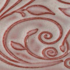 Close-up of a ceramic surface featuring intricate leaf and swirl patterns, glazed in a soft pink and red hue.