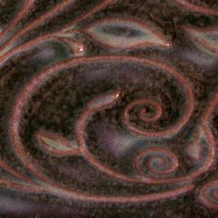 Dark clay surface with intricate swirling patterns in shades of brown, green, and hints of metallic highlights.