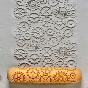 Textured clay surface featuring intricate gear designs pressed by a rubber rolling pin for ceramic decoration.